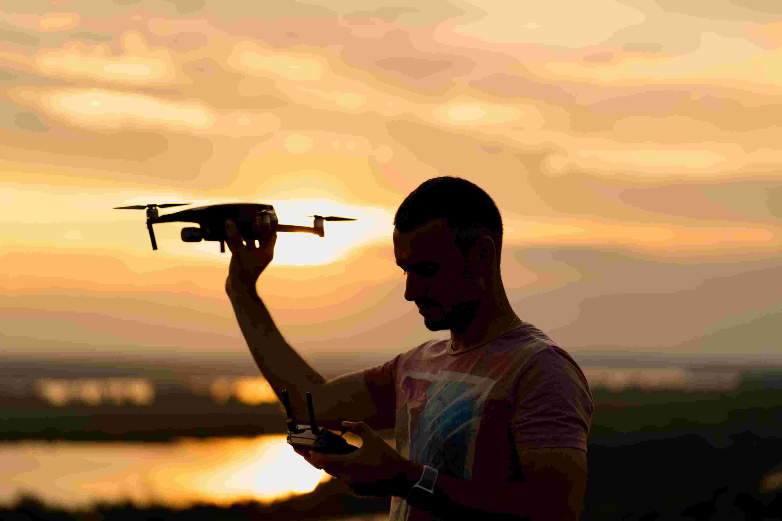 silhueta do homem pilotando um drone ao por do sol com ceu ensolarado no fundo